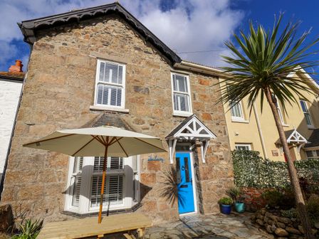 A stone house with a blue door a white umbrella and a palm tree outside at The Haven in Marazion