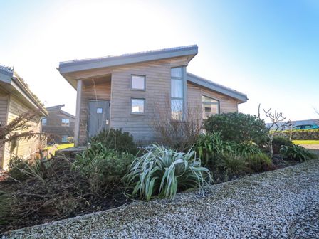 A wooden house with plants and gravel pathway outside at Una Lodge 77 in Carbis Bay