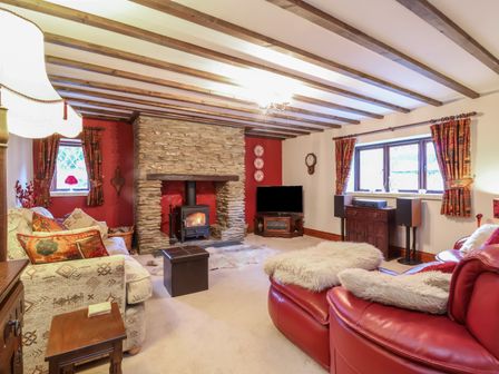 A living room with a stone fireplace a TV and sofas at Old Farm Cottage in Woolacombe