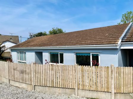 A single-story house with blue walls and brown roof behind a wooden fence at Trelawne Near Crackington Haven