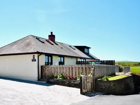A house with a tiled roof and fenced garden area with flowers and fields in the background at Penkenna in Crackington Haven