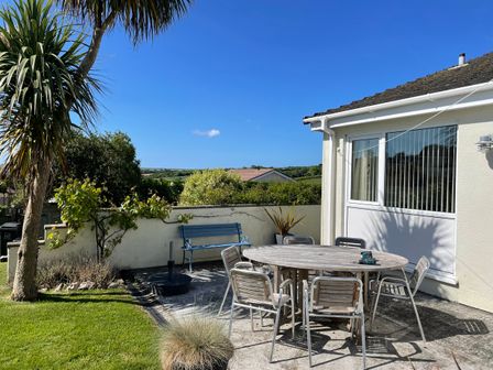 An outdoor patio with a wooden table and metal chairs near a cream-colored house with a window and a blue bench against a white wall at Maceley in Kingsbridge