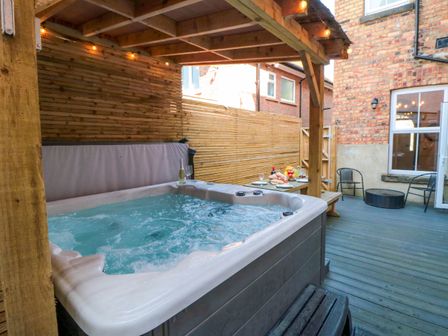 An outdoor area with a hot tub under a wooden pergola and a table set with food and drinks at Coronation House in Scarborough