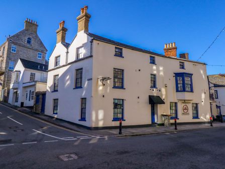 Street view of a white building with blue window frames on a corner at The Yardarm in Swanage