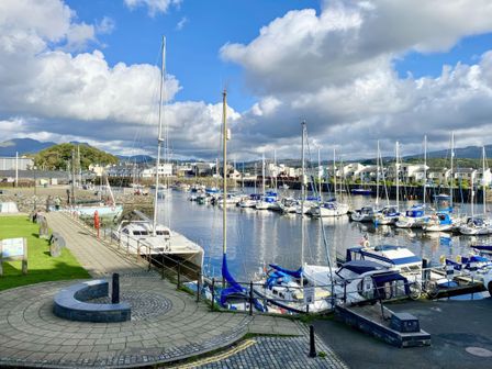 A marina with numerous sailboats and yachts docked along the water with buildings and hills in the background at Harbour Station View in Porthmadog