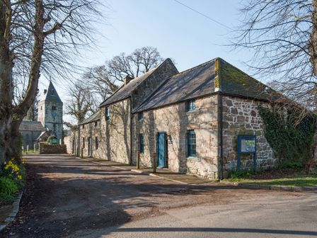 A stone building and church steeple with trees along the road at The Old Coach House Eglingham near Alnwick