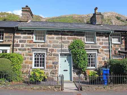 Stone cottage with a light blue door and windows with a mountain in the background at Ivy House in Beddgelert