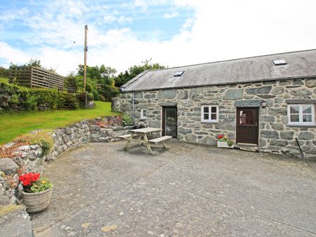 A stone building with a wooden door and window at Y Beudy The Old Byre in Llanbedr