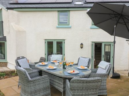 An outdoor patio with a dining table set with plates and glasses and surrounded by wicker chairs at Little Coombe in St Ann's Chapel