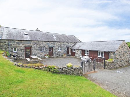 A stone cottage with a slate roof and patio furniture in a gated yard at Y Stabl The Old Stable in Llanbedr