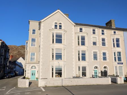 A row of multi-story residential buildings with bay windows and turquoise doors at Sandcastles in Barmouth