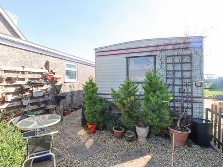 An outdoor area with a glass table and chairs next to potted plants and a caravan at Tanyfron Holiday Caravan in Bryngwran near Gwalchmai