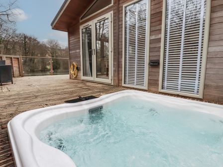 An outdoor deck with a bubbling hot tub near glass doors and windows at 2 Miller's Island Near Lanreath