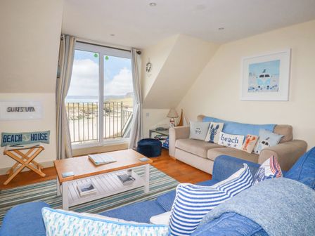 A living room with sofas cushions coffee table and a sliding glass door with a view of the beach at Driftwood in Newquay