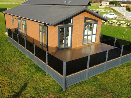 A wooden house with large windows and a fenced deck in a grassy area at Cherry Blossom Lodge in Whitby
