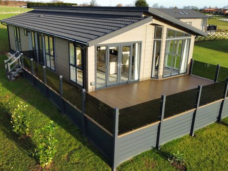 A modern single-story house with large windows and a patio surrounded by glass panels on a grassy lawn at Holly Lodge in Whitby