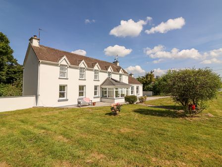 An exterior view of a two-story farmhouse with a grass lawn and bushes at Dromclough Farmhouse in Dromclough near Listowel County Kerry