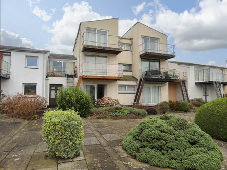 A residential building with balconies and a paved courtyard with shrubs at Clydfan in Porthmadog