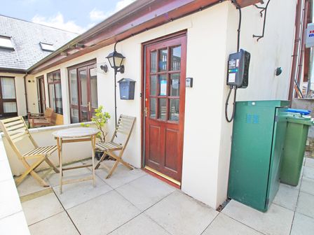 An outdoor patio area with two wooden chairs and a round table outside a red wooden door at Fisherman Cove in Porthmadog