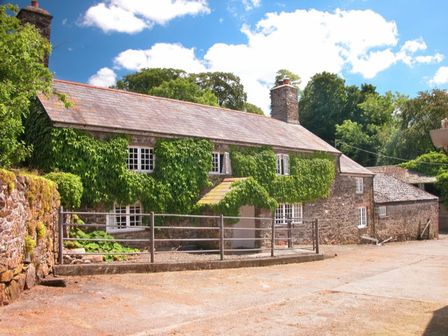 A stone house covered with ivy and a metal gate in front at The Farmhouse in Lydford