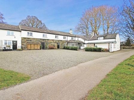 A gravel driveway leads to a white and stone building with multiple doors and windows surrounded by trees at Dowlais in Llanllyfni near Penygroes