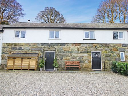 Exterior of a stone and white plaster building with black doors wooden bench and storage shed in a gravel yard at Igamogam in Llanllyfni near Penygroes