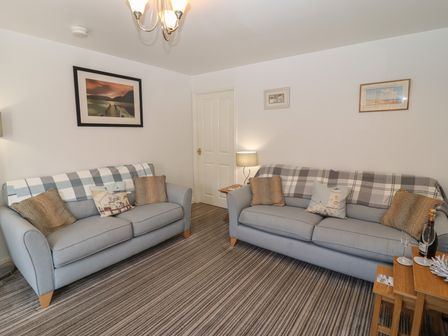 A living room with two sofas pillows framed pictures and a lamp at Pebble Cottage in Whitby