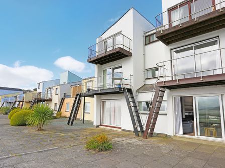 A row of modern townhouses with balconies and outdoor staircases on a paved sidewalk at 18D South Snowdon Wharf in Porthmadog