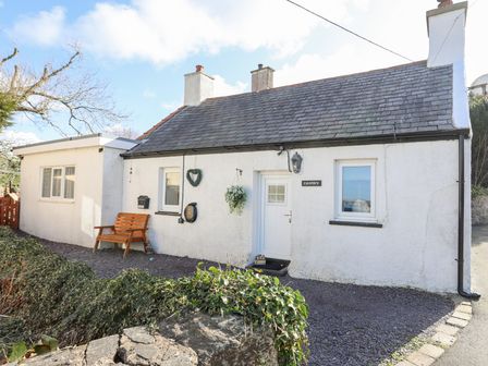 A white cottage with a grey shingle roof a wooden bench and hanging plants outside at Camwy in Brynsiencyn