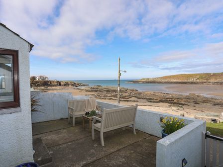 A patio with wooden benches and a table overlooking a rocky beach and the sea at 5 Sea View Street in Cemaes Bay