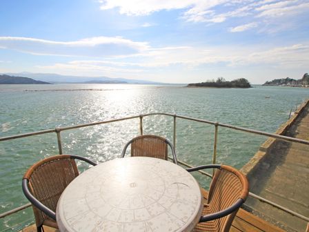A round table with four chairs on a balcony overlooking a body of water and an island at 11 South Snowdon Wharf in Porthmadog