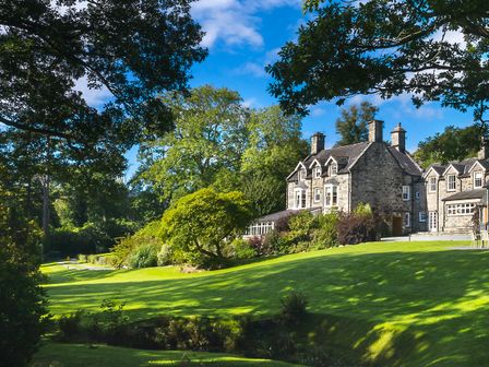 A stone house with multiple chimneys surrounded by trees and a lawn at Tan Llan in Llanelltyd near Dolgellau