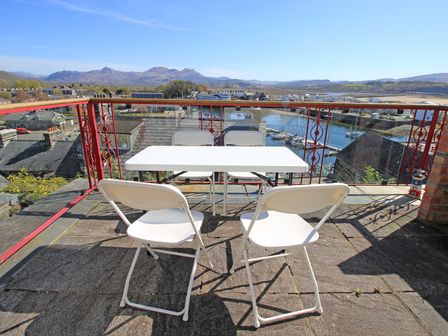 A rooftop patio with a white table and four white chairs overlooking a harbor and mountains at Captain Jack's in Porthmadog