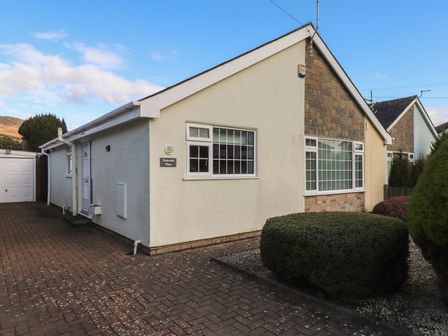 A single-story house with white walls and stone facade with windows and shrubs in front at Samson's Place in Morfa Bychan