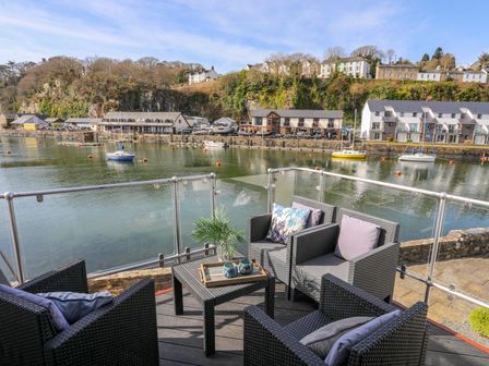A balcony with four chairs and a table overlooking a marina with boats and houses at Sailing Home in Porthmadog