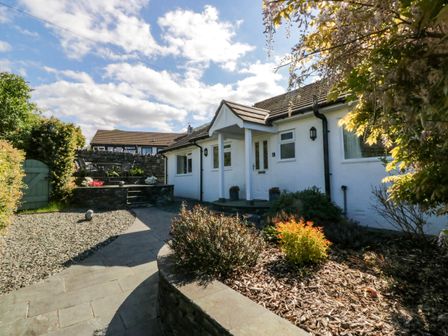 A pathway leading to a white house with a small porch and garden beds at Beckside in Ambleside