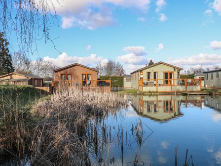 Two houses with wooden decks overlooking a pond with dry reeds at Stones Throw in Marston near Barkston