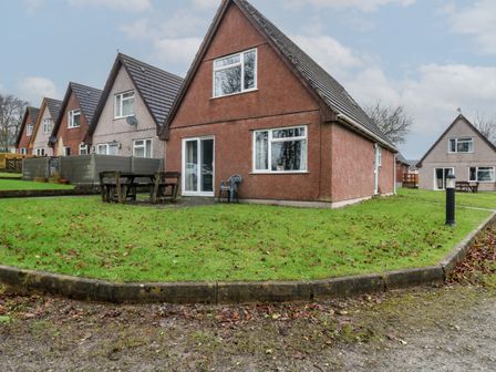 A row of triangular roof houses with grass lawns and outdoor furniture at Lewis Lodge in St Ann's Chapel
