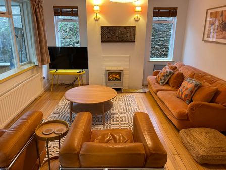 A living room with leather armchairs a sofa a round wooden coffee table a TV on a yellow stand and a fireplace at Lynchway in Lyme Regis