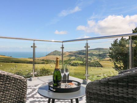 A balcony with two wicker chairs a small table with champagne and glasses overlooking hills and fields at Buddicombe House in Combe Martin