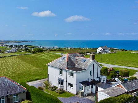 A white two-story house with a garden and picnic tables near the coastline at Glynmor in Llandanwg near Harlech