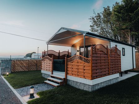 A small cabin with a covered porch and wooden fencing on grass at Benone Cabin in Magilligan near Castlerock