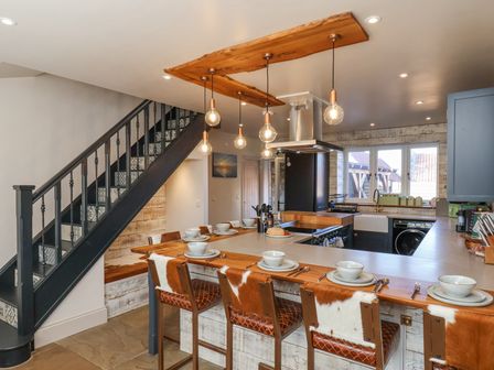 A kitchen with a wooden breakfast bar and cowhide chairs under hanging light bulbs at Beacon House in Sneaton