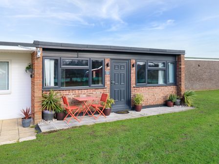 A small brick house with black framed windows red chairs and table and several potted plants outside at 271 California Sands Estate in California Norfolk