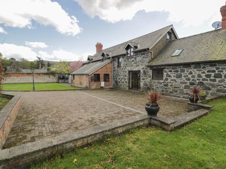 An outdoor paved patio area with two potted plants adjacent to a stone and brick house at Y Granar in Conwy
