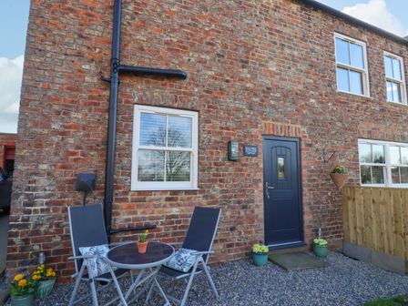 A brick exterior of a cottage with a blue door two patio chairs and a round table with potted plants at Elm Tree Cottage Dalton Near Thirsk