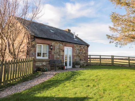 A stone cottage with a bench and gravel path in front of a fenced grassy yard at The Forge Nr Seashouses
