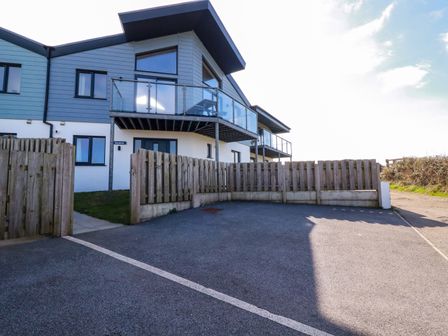 A modern house with a balcony and glass railing behind a wooden fence and driveway at Jacana in Perranporth