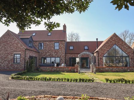 A brick house with tiled roof and large windows in a garden with a gravel driveway at Crossett Grange in Driffield