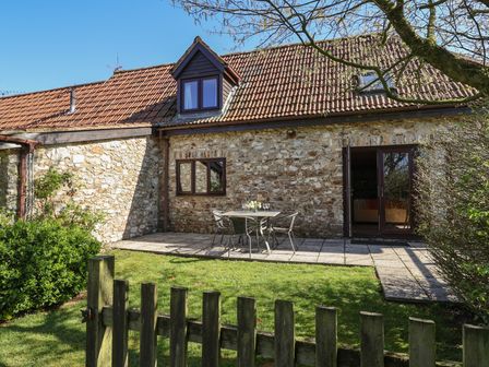 A stone exterior cottage with a tiled roof a gated lawn and a patio table with four chairs at Meadow Cottage in Upottery